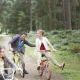 Rodzina na rowerach w lesie, śmieją się i cieszą wspólnym czasem. Może to być wycieczka w okolice zalewu wolbromskiego.