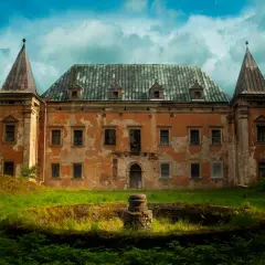 Zrujnowany pałac z wieżyczkami, porośnięty mchem i otoczony bujną zielenią. Kruszyna historii w zapomnianym miejscu.