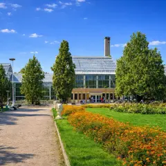 Okrąglak Poznań w słoneczny dzień, z kwitnącymi rabatami kwiatowymi i zielenią.