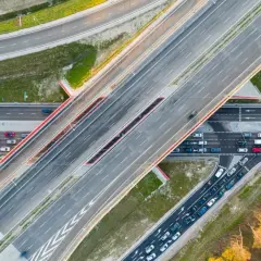 Widok z lotu ptaka na wielopasmową drogę, która może być najdłuższą ulicą w Warszawie. Samochody poruszają się po betonowych pasach.