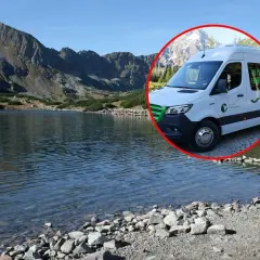 Biały bus do Morskiego Oka stoi przy tafli jeziora, w tle góry.