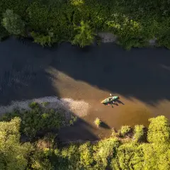 Dwie osoby płyną kajakiem po rzece w pobliżu Frysztaka, otoczeni bujną zielenią.