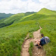 Turysta odpoczywa na szlaku w Bieszczadach, gdzie leżą zielone połoniny i malownicze wzgórza.
