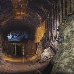 Wnętrze kopalni, drewniane obudowy tunelu, skalne ściany i ciemność. Gdzieś w oddali widać wejście do dalszej części korytarza, jakby otwarta **osowka**.