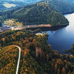 Malownicza zapora wodna w Zagórzu Śląskim otoczona jesiennymi lasami. Kręta droga prowadzi do urokliwego ośrodka wypoczynkowego nad spokojną taflą jeziora.