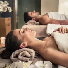Para relaksu w spa: para leży na stołach do masażu, otoczona świecami i kwiatami. To idealne miejsce, by zapomnieć o codzienności.