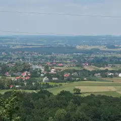 Widok na malowniczą wieś Przytkowice z kościołem w centrum, otoczoną zielonymi wzgórzami i polami.