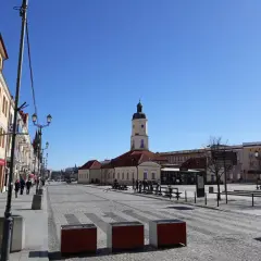 Słoneczny dzień na Rynku Kościuszki w Białymstoku. W oddali wieża ratusza, po bokach kamienice i brukowana nawierzchnia.