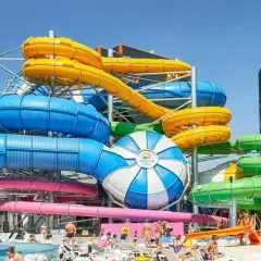 Kolorowe zjeżdżalnie wodne w jednym z najlepszych aquaparków w Polsce. W tle widać ludzi odpoczywających na leżakach.
