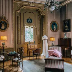 Eleganckie wnętrze pałacu w Nieborowie z portretami dam, manekinem w sukni i zabytkowymi meblami.