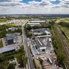 Widok z lotu ptaka na przemysłową okolicę z magazynami, torami kolejowymi i drogą. W oddali widać miasto. To miejsce, gdzie psy mają swoje psie pole.