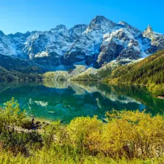 Morskie Oko, Tatry. Turkusowa tafla jeziora odbija ośnieżone szczyty. Widoczna głębokość wody i jesienna roślinność.