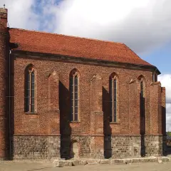 Gotycka budowla z cegły, przypominająca dawną warownię templariuszy, z charakterystyczną okrągłą wieżą i strzelistymi oknami.