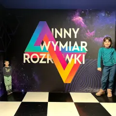 Dzieci w "Innym Wymiarze Rozrywki" w Warszawie. Kolorowa ściana z motywem kosmosu i geometrycznymi kształtami.