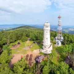 Kamienna wieża widokowa i maszt telekomunikacyjny na zalesionym szczycie góry.