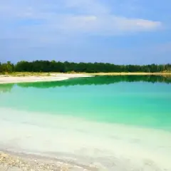 Piękne, turkusowe jezioro lazurowe odbija zielony las i błękitne niebo. Biały piasek na brzegu tworzy kontrast.
