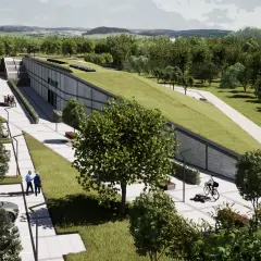 Nowoczesny budynek z zielonym dachem wkomponowany w krajobraz. Obok parking, chodnik z ławkami i ścieżka rowerowa. W tle las i wzgórza.
