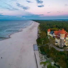 Zachód słońca nad morzem w Łebie. Piękna plaża, las i zabytkowy budynek przypominający zamek.