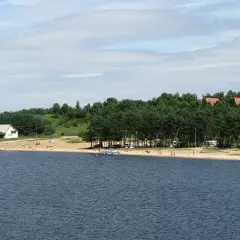 Słoneczny dzień nad zalewem Chańcza. Plaża z ludźmi, domki letniskowe i las.