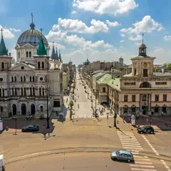 Widok na plac wolności w Łodzi z monumentalną katedrą po lewej i długą ulicą pełną ludzi i samochodów.