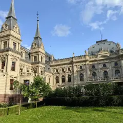 Imponujący pałac poznańskiego, z wieżyczkami i bogatymi zdobieniami, otoczony zielonym ogrodem z kwitnącymi krzewami róż.
