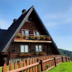 Drewniane schronisko na Maciejowej z kwitnącymi pelargoniami na balkonach i oknach. Otoczone zielenią i lasem, zaprasza na górskie wędrówki.