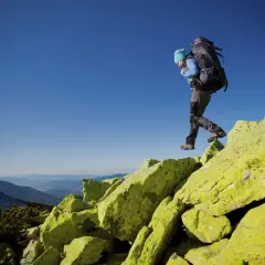 Turysta z plecakiem pokonuje skaliste zbocze. W tle rozciągają się malownicze **beskid żywiecki szczyty**.