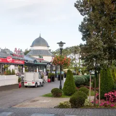 Spacer po alei gwiazd w Międzyzdrojach, z restauracjami i kawiarniami po lewej stronie, a zielenią i drzewami po prawej.