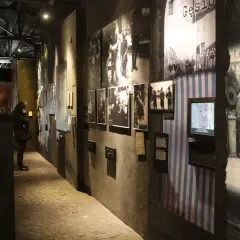 Wystawa w Muzeum Powstania Warszawskiego. Zwiedzający wpatrują się w historyczne fotografie i eksponaty, które budzą refleksje.