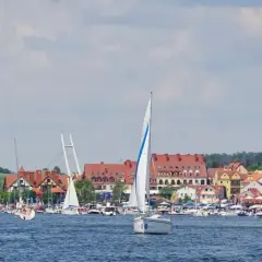 Żaglówki na błękitnych jeziorach na Mazurach, z malowniczym miasteczkiem w tle.