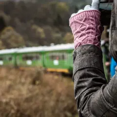 Osoba w różowych rękawiczkach fotografuje zielono-czerwony pociąg. Która kolejka bieszczadzka, która trasa ciekawsza?