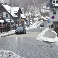 Zimowy deptak w Szklarskiej Porębie z samochodami na ulicy i sklepikami z pamiątkami.