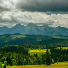 Majestatyczny szczyt w Tatrach Zachodnich, otoczony zielonymi lasami i polami, pod burzowymi chmurami.