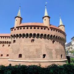 Krakowski zabytek przy Bramie Floriańskiej, okrągła baszta obronna z cegły, góruje nad zielonymi terenami i ulicą.