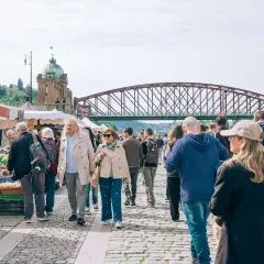 Tłum ludzi na targu, most w tle. Może to być scena z jednego z miast w rankingu miast w Polsce.