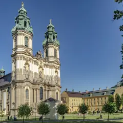 Barokowy zespół klasztorny w Krzeszowie z dwiema wieżami i rozległym skrzydłem, otoczony zielenią.