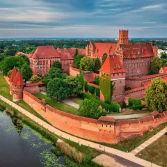Malbork, największy zamek w Polsce, majestatycznie wznosi się nad rzeką Nogat. Potężne ceglane mury i liczne wieże świadczą o jego bogatej historii.