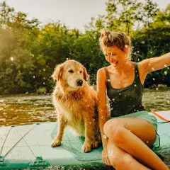 Radosna dziewczyna i jej pies na desce SUP na jeziorze. Idealne miejsce, gdzie na wakacje z psem w Polsce.