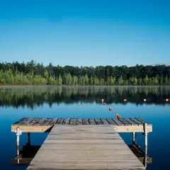Drewniany pomost na spokojnym jeziorze, otoczony lasem. Idealny poraj na poranne wędkowanie lub relaks.