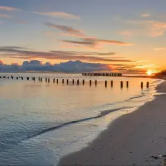 Zachód słońca nad spokojnym morzem, z rzędem drewnianych słupków na plaży w Słajszewie.