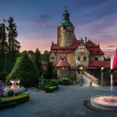Zamek Czocha o zmierzchu, z fontannami i kwitnącymi rododendronami. Bilety do zamku można kupić online lub na miejscu.