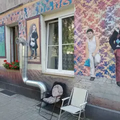 Kolorowe murale z postaciami dzieci i wzorami zdobią kamienicę na Nadodrzu. Dwa krzesła stoją przed ścianą.