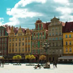 Kolorowe kamienice na starym rynku we Wrocławiu, z błękitnym niebem i białymi chmurami w tle.