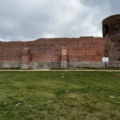 Ruiny ceglanego zamku w Kole, z charakterystyczną okrągłą wieżą, stoją na tle pochmurnego nieba.