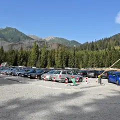 Parking pod Morskim Okiem, pełen samochodów, z górami i lasem w tle.