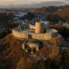 Zamek w Rytrze, kamienne ruiny na wzgórzu, z widokiem na dolinę i rzekę. Flaga Polski powiewa na wieży.