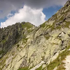 Kamienista ścieżka wije się po zboczu górskim, prowadząc w stronę skalistych szczytów. Widok na Szpiglasową Przełęcz, gdzie chmury przecinają błękit nieba.