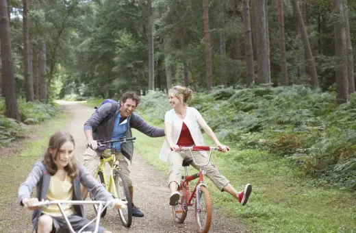 Rodzina na rowerach w lesie, śmieją się i cieszą wspólnym czasem. Może to być wycieczka w okolice zalewu wolbromskiego.