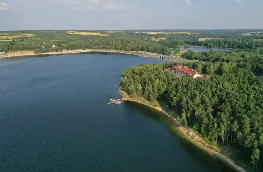Malownicze jezioro Chańcza otoczone lasem, z hotelem i pomostem.
