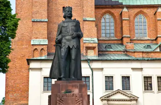 Pomnik Bolesława Chrobrego, pierwszego króla polskiego, na tle ceglanej katedry.